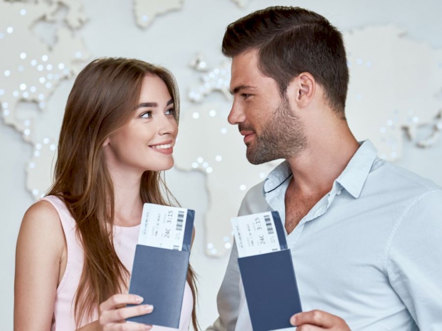 Joyful couple looking to each other and holding passport with flying tickets