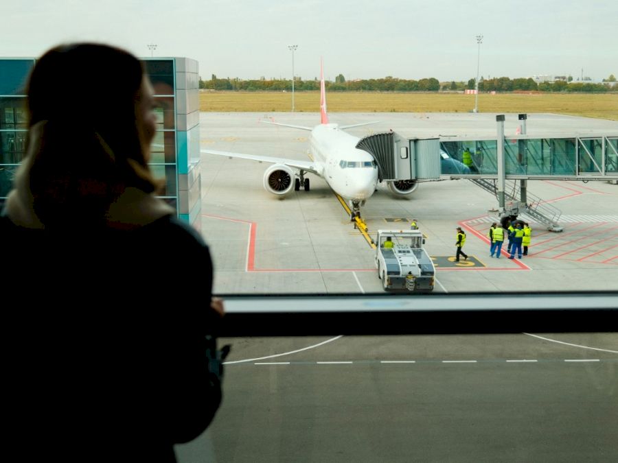 Woman traveler standing near panoramic big window at airport. Lady waiting for flight. Travel, journey, airplane concept.